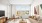 View of a staged living room with tan couch, coffee table, entertainment cabinet with tv, wooden chair and oversized windows showcasing fall foliage at The Prescott at Concord